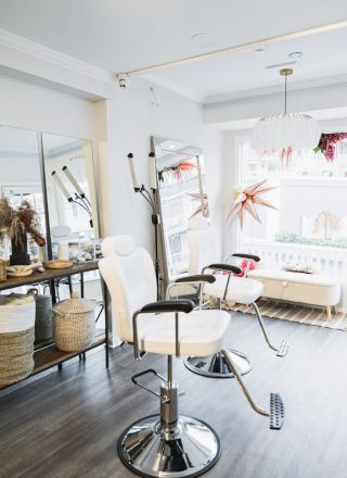 The image shows a modern, bright salon with styling chairs, large mirrors, and a decorative console with baskets, set against a large window with white curtains.