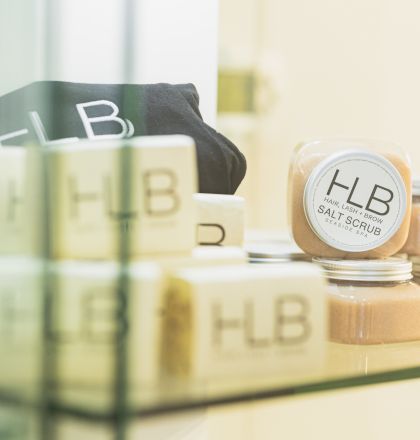 The image shows jars of HLB salt scrub and HLB branded items on a glass shelf, including some black and white packaging, arranged neatly.