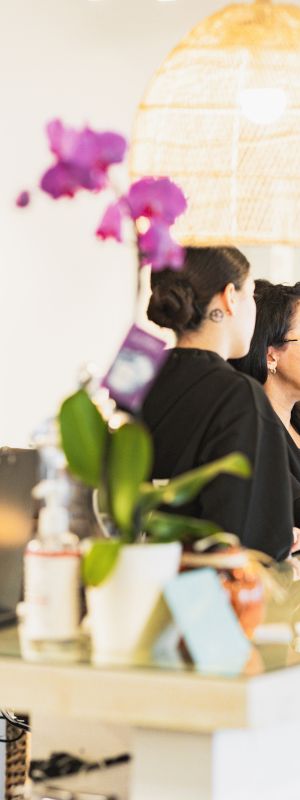 People at a reception desk, decorated with plants and pendant lights, appear to be engaging in conversation.