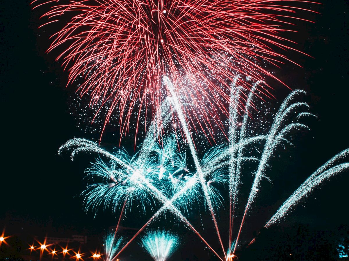 The image shows colorful fireworks exploding in the night sky, with their reflections visible in the water below, creating a vibrant display.