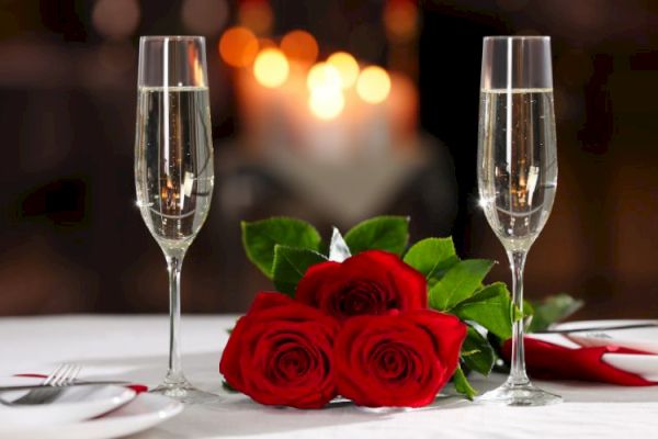 A romantic setup with two champagne glasses, three red roses, and a blurred background with warm lights.