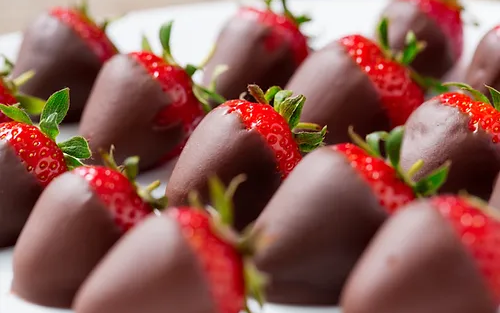 The image shows several strawberries partially dipped in chocolate, arranged neatly on a white surface.