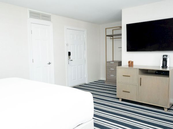 A bright hotel room with two white doors, a dresser, flat-screen TV, and a Keurig coffee maker on the counter.