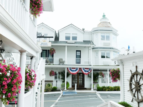 A charming white building with balconies, flower baskets, and a ship wheel decoration, adorned with red, white, and blue bunting for decoration.