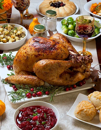A Thanksgiving feast with a roasted turkey, vegetables, cranberry sauce, rolls, and autumn decorations on a table.
