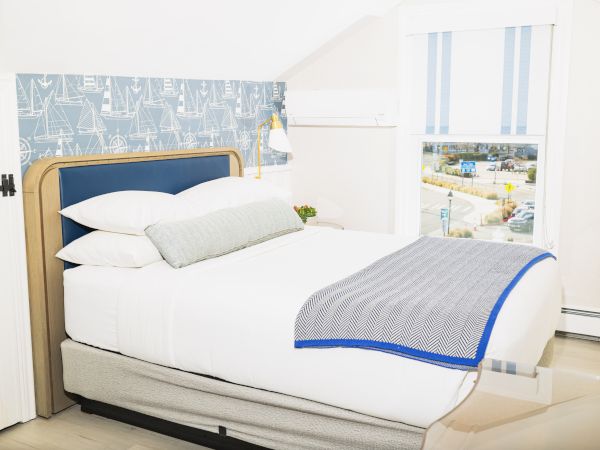 The image shows a tidy bedroom with a neatly made bed, blue and white décor, and a window overlooking an outdoor scene, ending the sentence.