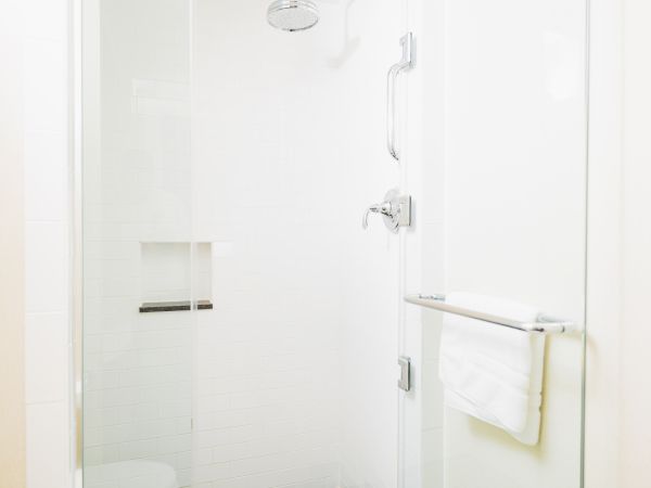 This image shows a clean, white shower stall with a glass door, a towel hanging on a bar, and a showerhead and control handle on the wall.