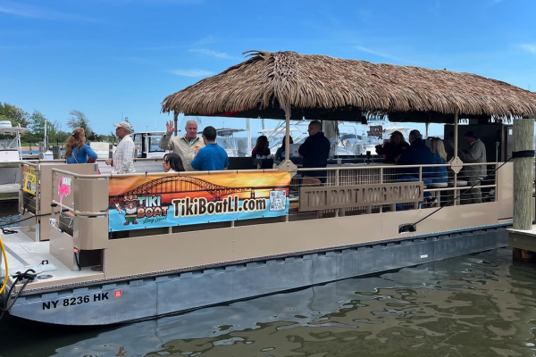 A tiki-themed boat with people on board is docked at a pier under a clear blue sky.
