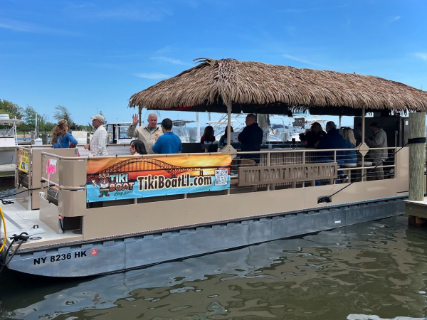 A tiki-themed boat with people on board is docked at a pier under a clear blue sky.