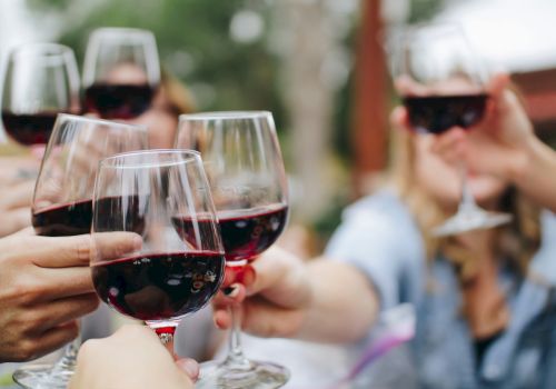 People raising glasses of red wine in a toast, celebrating together outdoors with a blurred background.