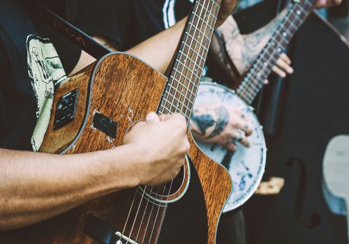 Two people are playing musical instruments: one with a guitar and the other with a banjo, showcasing a street performance.