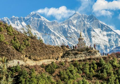 A mountain landscape features a stupa on a hill, with snow-capped peaks and clear skies in the background.