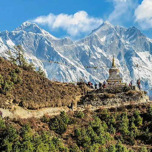 A mountain landscape features a stupa on a hill, with snow-capped peaks and clear skies in the background.