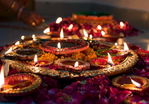 Decorative arrangement of lit oil lamps with surrounding flowers, creating a warm and festive ambiance.