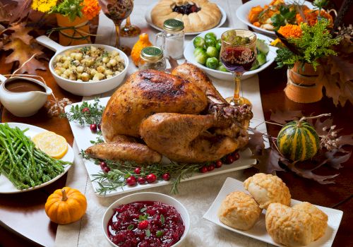 A Thanksgiving feast with a roasted turkey, side dishes, cranberry sauce, bread rolls, and autumn decorations on a table.