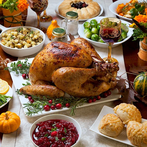 A Thanksgiving feast with a roasted turkey, side dishes, cranberry sauce, bread rolls, and autumn decorations on a table.