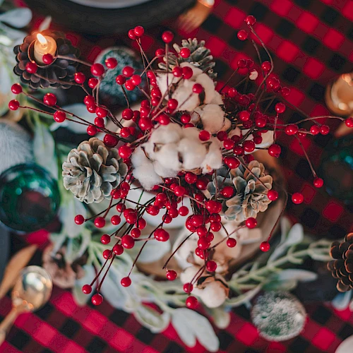 A festive table centerpiece with red berries, pinecones, and a cozy plaid setting.