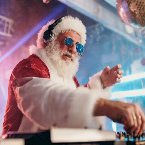 Santa wearing headphones and sunglasses, DJing at a festive party with disco lights and a glittery backdrop.