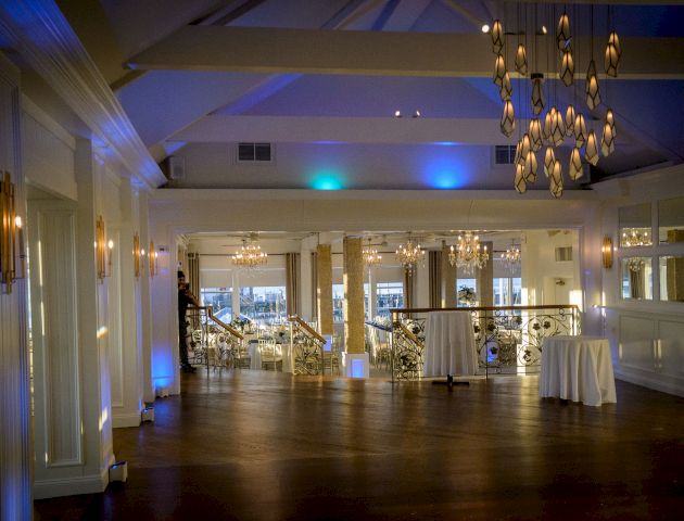 A cozy restaurant lobby with warm lighting, wooden floor, and a welcoming bar area; people mingle near the front desk, ceiling lanterns.