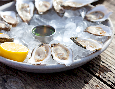 Oysters on ice with lemon wedges and a small sauce cup, served on a rustic wooden table.