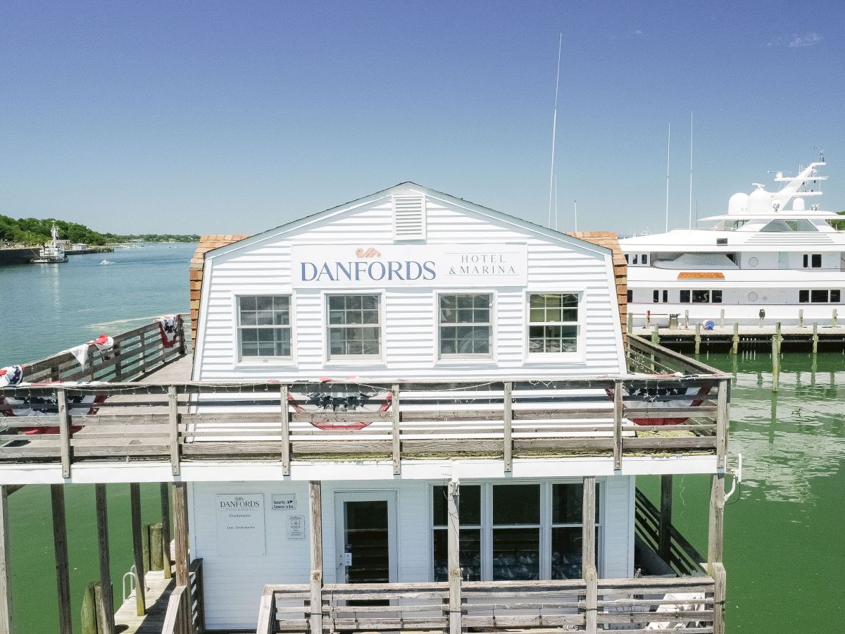 A &ldquo;Danfords Hotel & Marina&rdquo; dock building sits on a river, with a large yacht and calm water in the background.
