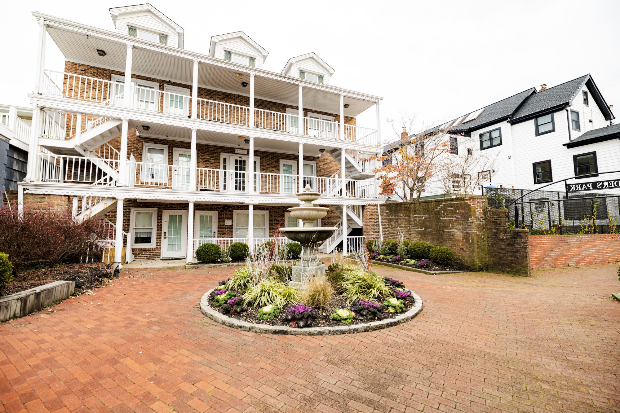 A three-story building with balconies, a circular fountain garden in front, and another house on the right side completes the scene.